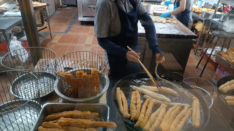 早餐店廚房裡，戴口罩的店員用長筷子翻炸油條